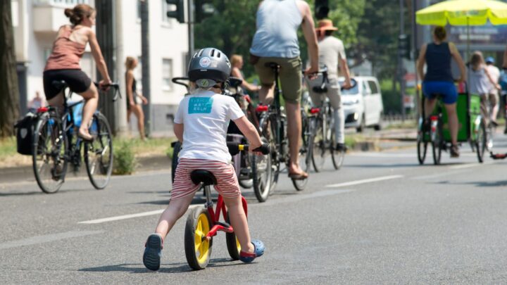 Kind auf Laufrad, im Hintergrund einige Fahrradfahrer:innen